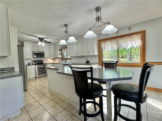 kitchen with stainless steel appliances, light tile patterned flooring, white cabinetry, hanging light fixtures, and decorative backsplash