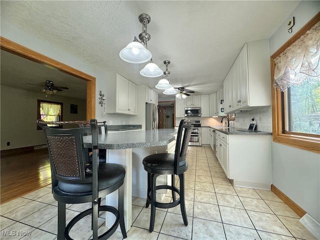 kitchen with stainless steel appliances, white cabinetry, sink, and decorative light fixtures