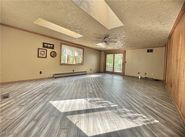 unfurnished room with a baseboard radiator, wood-type flooring, a textured ceiling, wooden walls, and a skylight