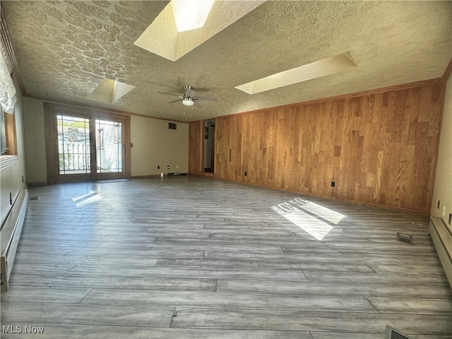 empty room featuring a textured ceiling, wooden walls, light wood-type flooring, and a skylight