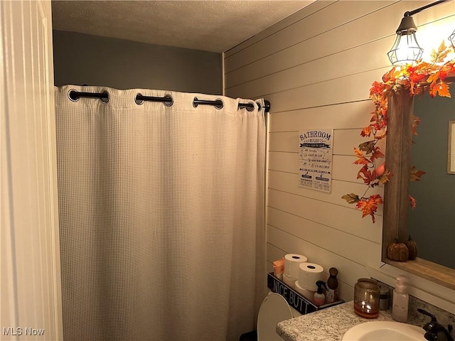 bathroom with a textured ceiling, toilet, wooden walls, and sink