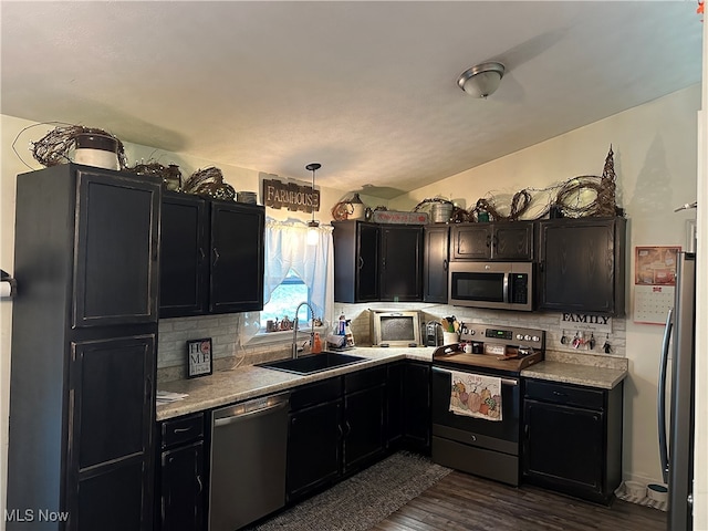 kitchen featuring decorative backsplash, appliances with stainless steel finishes, dark wood-type flooring, sink, and hanging light fixtures