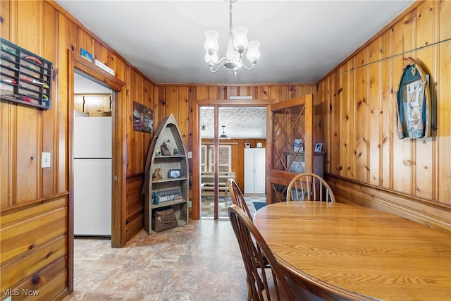 dining space with crown molding, wooden walls, and an inviting chandelier