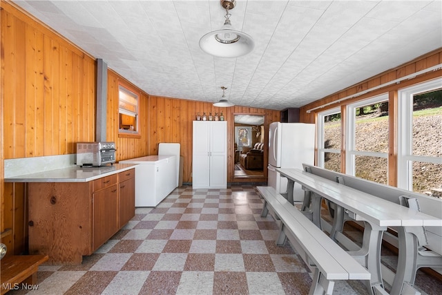 kitchen featuring white refrigerator, hanging light fixtures, wood walls, and a wood stove