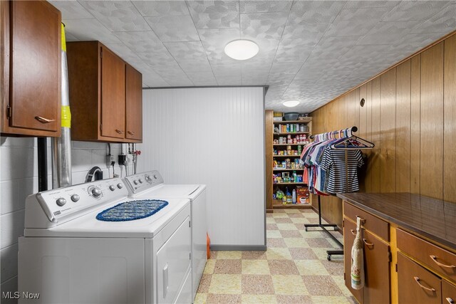 laundry area featuring cabinets, wood walls, and separate washer and dryer