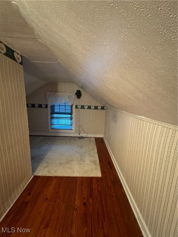 additional living space with a textured ceiling, vaulted ceiling, and hardwood / wood-style flooring