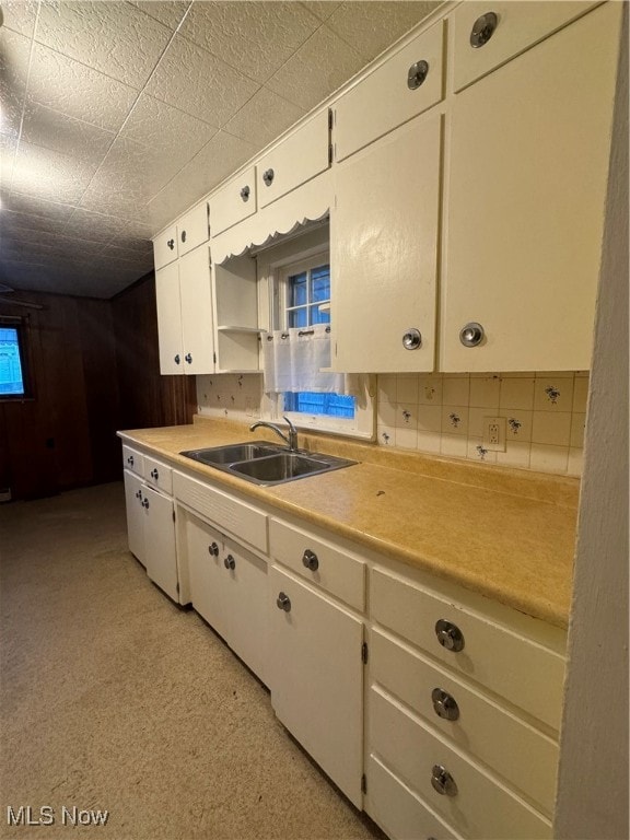 kitchen with white cabinets, wood walls, and sink