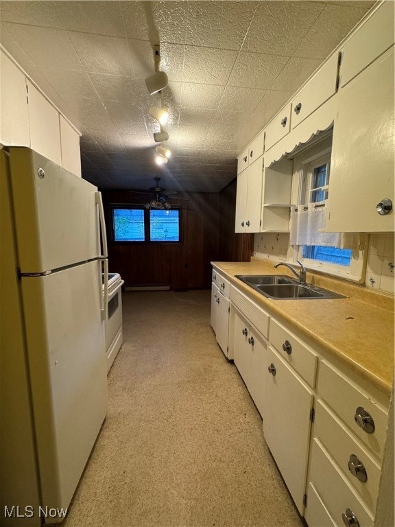 kitchen with sink, wood walls, white cabinetry, white appliances, and ceiling fan