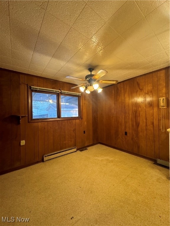 carpeted spare room featuring wooden walls, baseboard heating, and ceiling fan