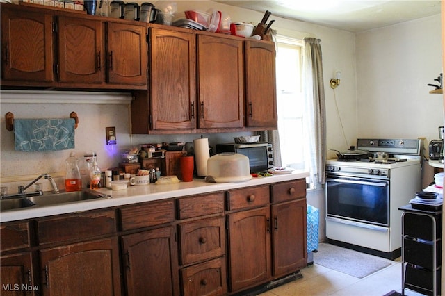 kitchen featuring white gas range oven, light tile patterned floors, and sink