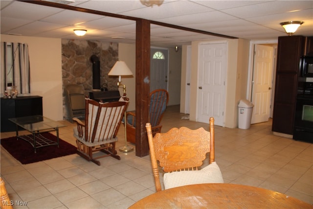 living room featuring a drop ceiling, light tile patterned flooring, and a wood stove