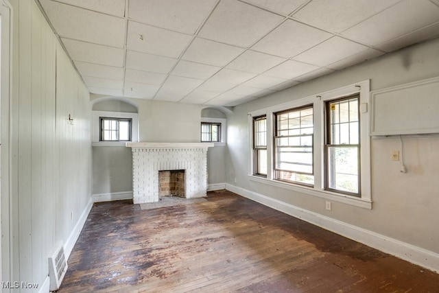 unfurnished living room featuring plenty of natural light, dark wood-type flooring, and a brick fireplace