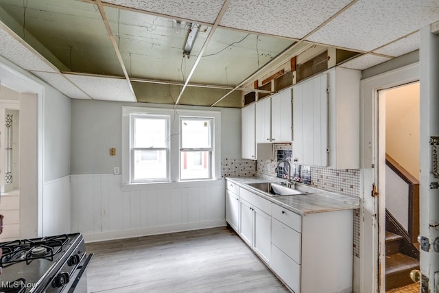 kitchen with sink, a paneled ceiling, white cabinetry, light wood-type flooring, and decorative backsplash