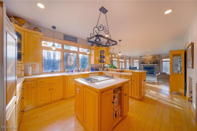 kitchen with pendant lighting, a center island, stainless steel gas stovetop, a fireplace, and light hardwood / wood-style flooring