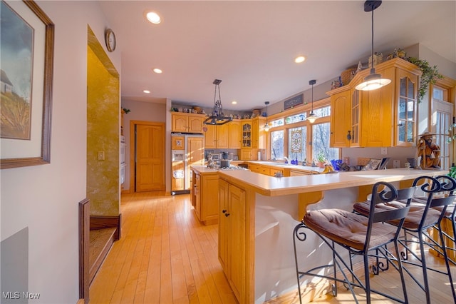 kitchen with light hardwood / wood-style floors, kitchen peninsula, a breakfast bar area, and light brown cabinets