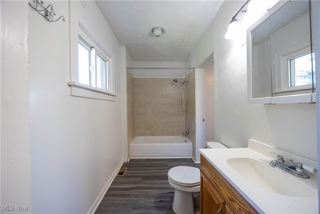 full bathroom featuring wood-type flooring, vanity, tiled shower / bath, and toilet