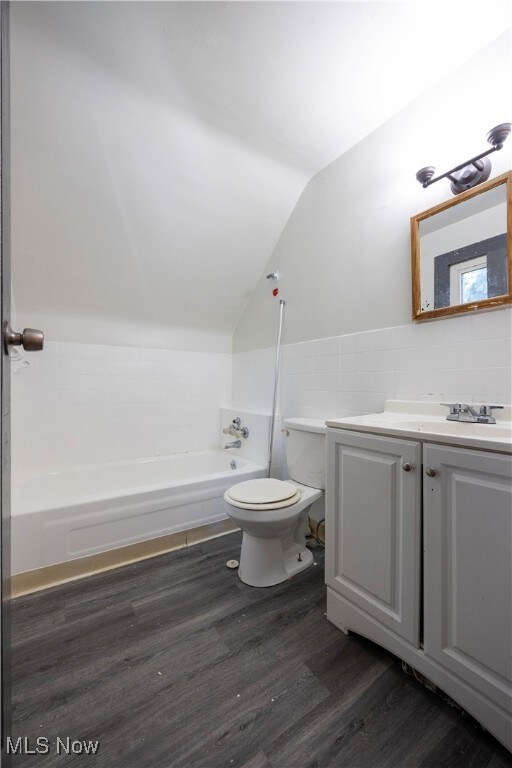 bathroom featuring wood-type flooring, toilet, lofted ceiling, vanity, and a bathing tub