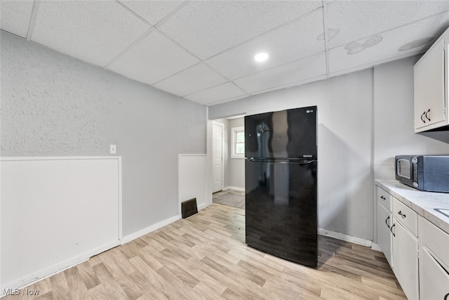 kitchen featuring white cabinets, light wood-type flooring, a drop ceiling, and black appliances