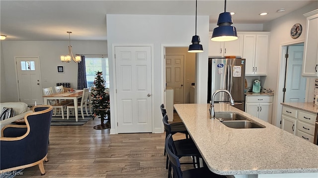 kitchen with stainless steel fridge, a kitchen island with sink, sink, and white cabinets