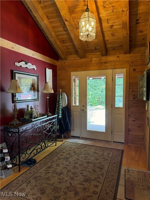 entrance foyer with vaulted ceiling with beams, wood walls, light tile patterned floors, wooden ceiling, and an inviting chandelier