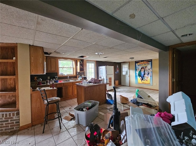 interior space with a drop ceiling, a kitchen island, light tile patterned floors, and sink