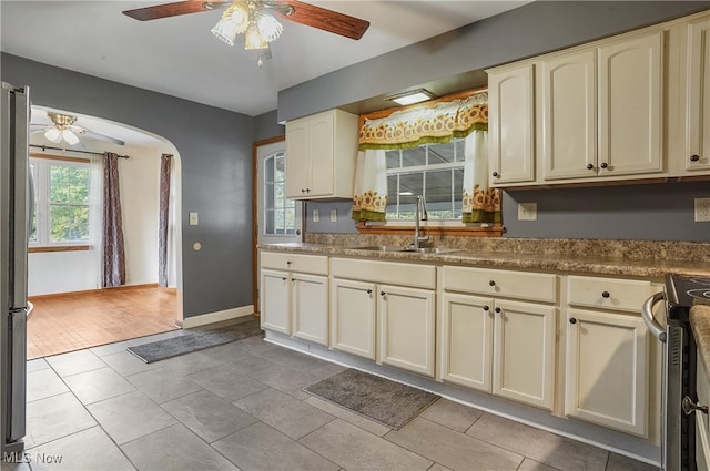 kitchen with cream cabinetry, stainless steel stove, ceiling fan, light hardwood / wood-style flooring, and sink