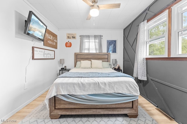 bedroom featuring ceiling fan, light hardwood / wood-style flooring, ornamental molding, and multiple windows