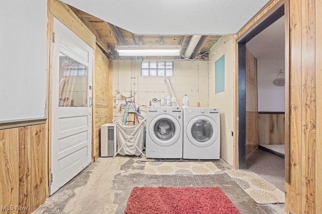 clothes washing area featuring washing machine and clothes dryer, wood walls, and a textured ceiling