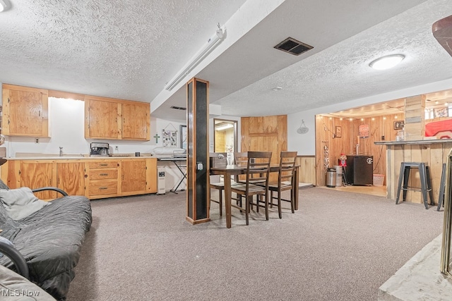 kitchen featuring a textured ceiling, kitchen peninsula, light colored carpet, a kitchen bar, and wooden walls