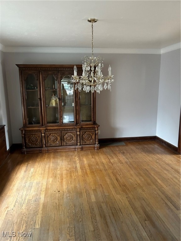 unfurnished dining area with a notable chandelier, hardwood / wood-style floors, and crown molding