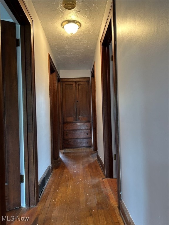 corridor with a textured ceiling and dark hardwood / wood-style floors