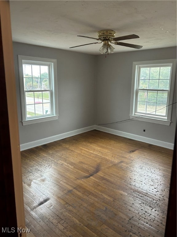 empty room with ceiling fan, dark hardwood / wood-style floors, and a healthy amount of sunlight