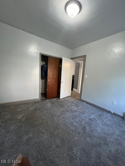 unfurnished bedroom with dark colored carpet and a closet