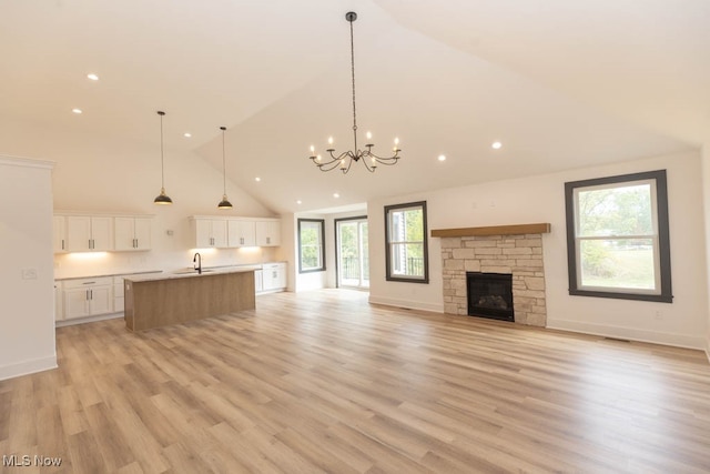 kitchen with light hardwood / wood-style flooring, a large island with sink, white cabinetry, an inviting chandelier, and a fireplace