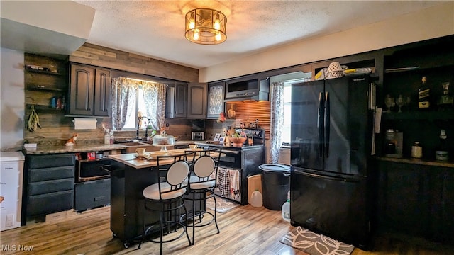 kitchen featuring a breakfast bar area, light wood-type flooring, a center island, dark brown cabinets, and black fridge