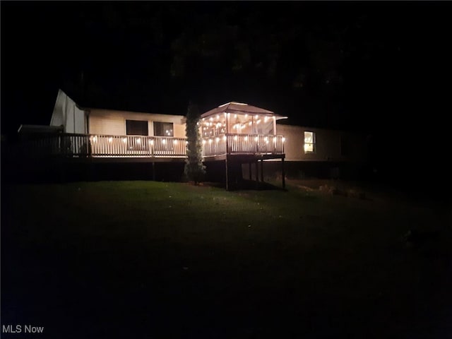 back house at twilight with a lawn and a deck