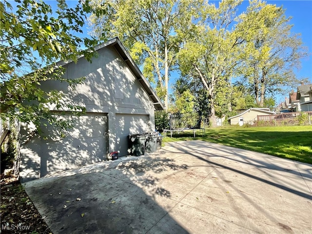 view of property exterior with a trampoline, a garage, and a lawn