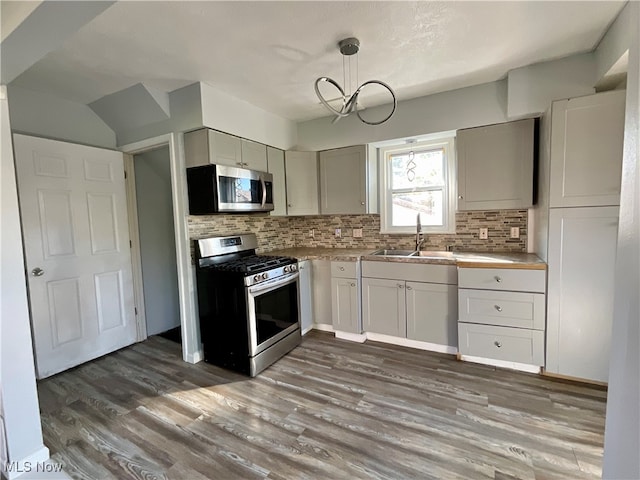 kitchen with tasteful backsplash, hanging light fixtures, dark hardwood / wood-style floors, sink, and stainless steel appliances