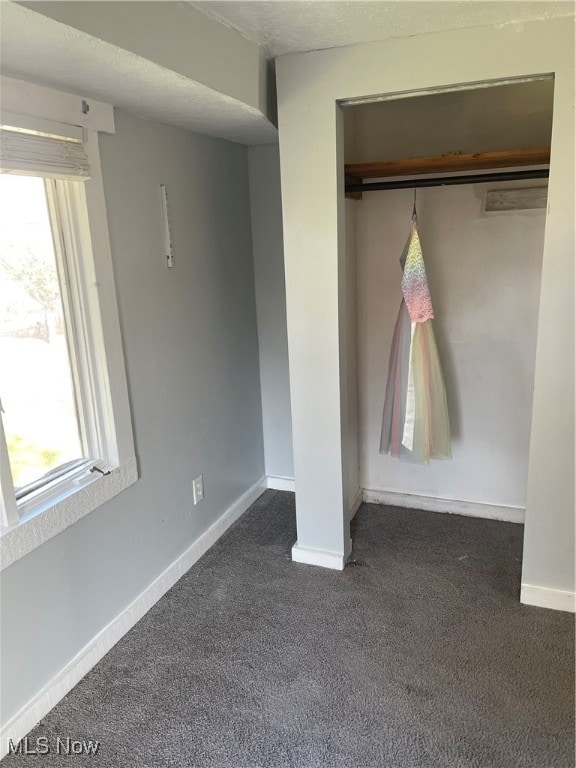 unfurnished bedroom with a closet, a textured ceiling, and dark carpet