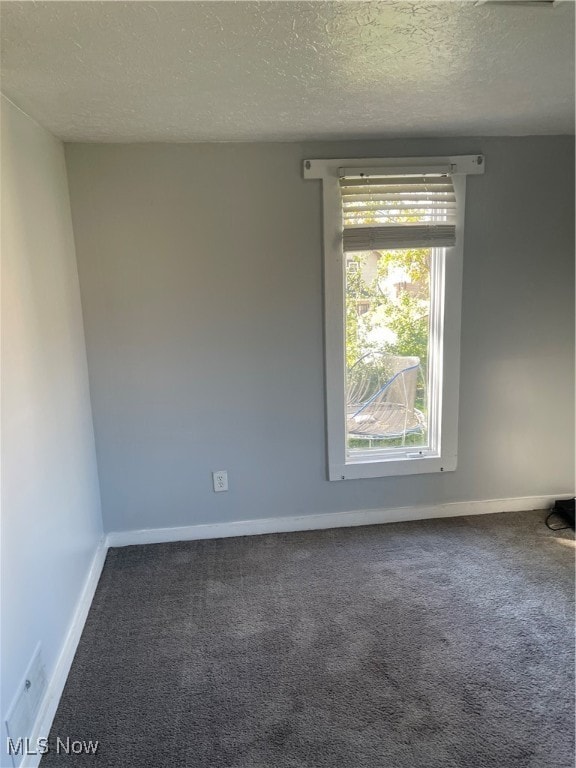 unfurnished room featuring a textured ceiling and dark colored carpet