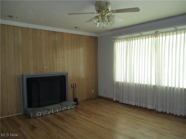 unfurnished living room featuring ceiling fan, hardwood / wood-style flooring, wood walls, and crown molding