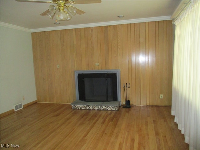 unfurnished living room with ceiling fan, wooden walls, ornamental molding, and wood-type flooring