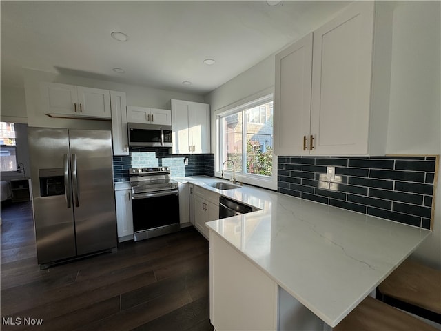 kitchen with sink, kitchen peninsula, white cabinetry, stainless steel appliances, and dark hardwood / wood-style flooring