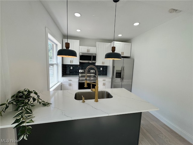 kitchen with appliances with stainless steel finishes, hanging light fixtures, white cabinetry, and light stone countertops