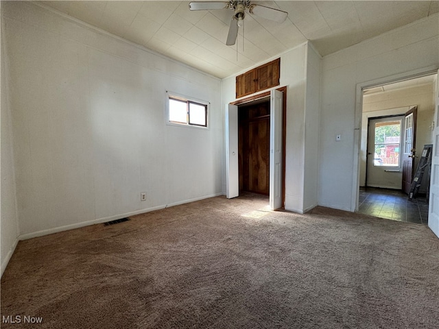 unfurnished bedroom featuring dark carpet, multiple windows, and ceiling fan