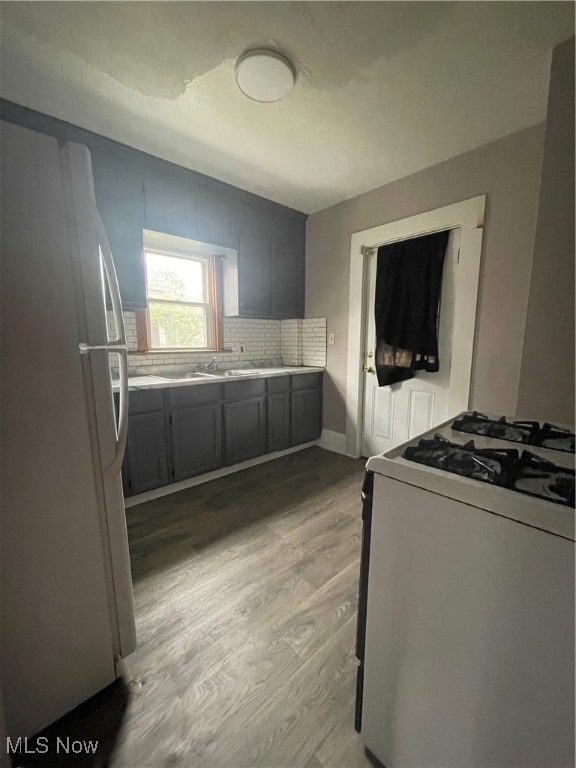 kitchen with gray cabinetry, white appliances, backsplash, and light hardwood / wood-style flooring