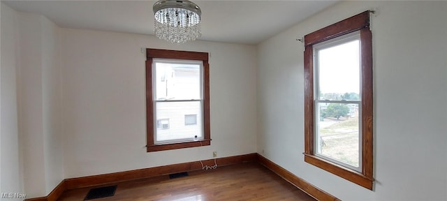 empty room featuring a notable chandelier and wood-type flooring