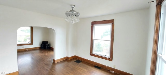 empty room featuring a notable chandelier, dark hardwood / wood-style flooring, and a wealth of natural light