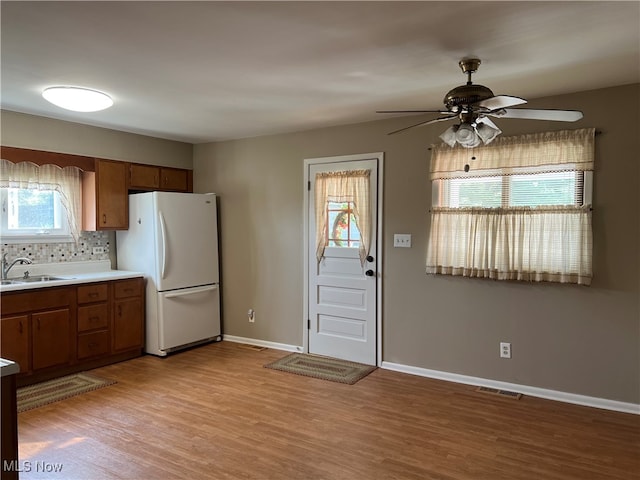 kitchen featuring light wood-type flooring, white refrigerator, sink, backsplash, and ceiling fan