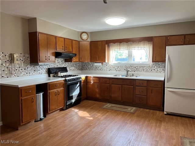 kitchen with sink, white fridge, light hardwood / wood-style flooring, decorative backsplash, and black range with gas stovetop